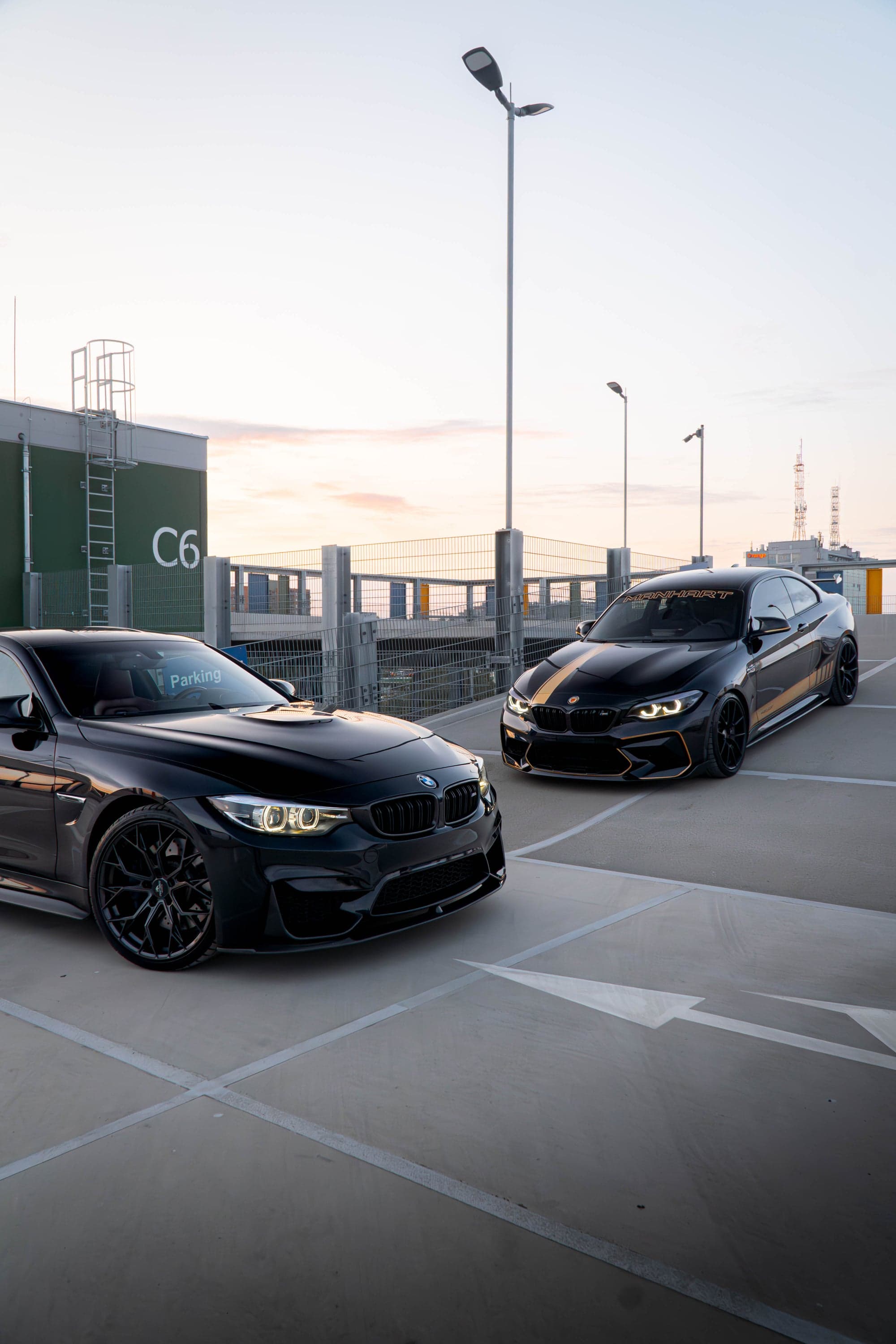Dwa czarne BMW na parkingu o zachodzie słońca